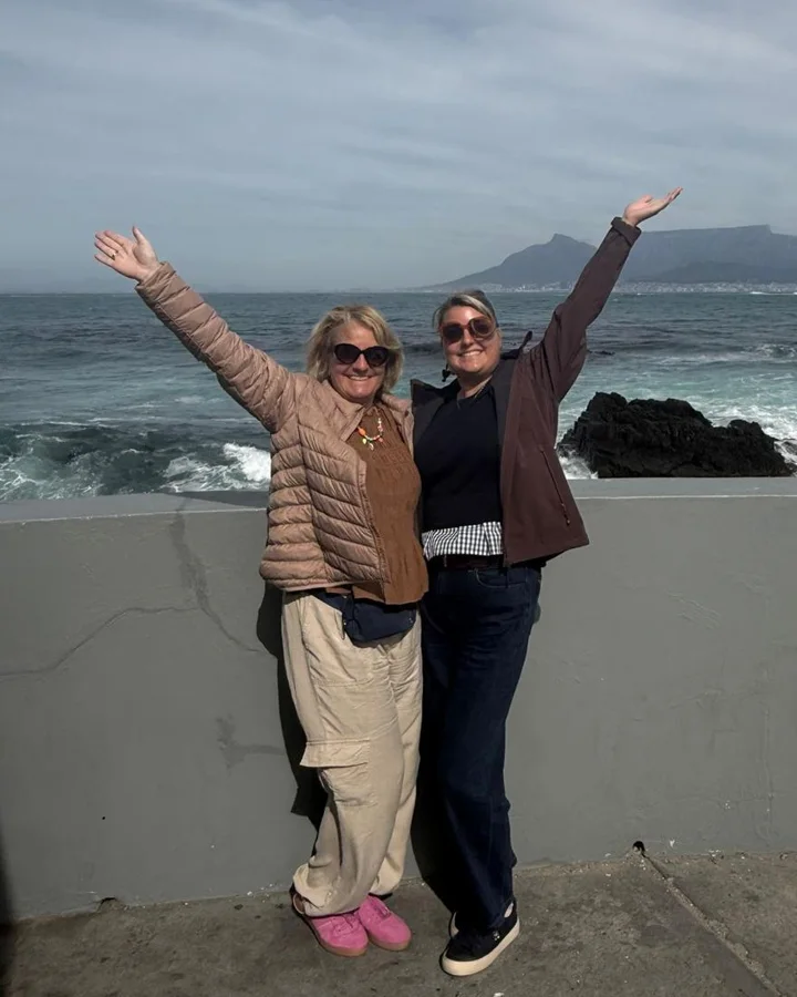 Joyce en Mirte met de armen omhoog aan zee, met de Tafelberg op de achtergrond