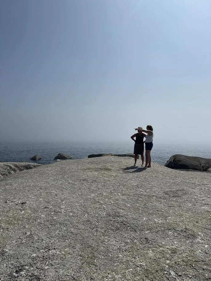 Moeder en dochter op de rotsen aan zee, de dochter wijst naar de horizon